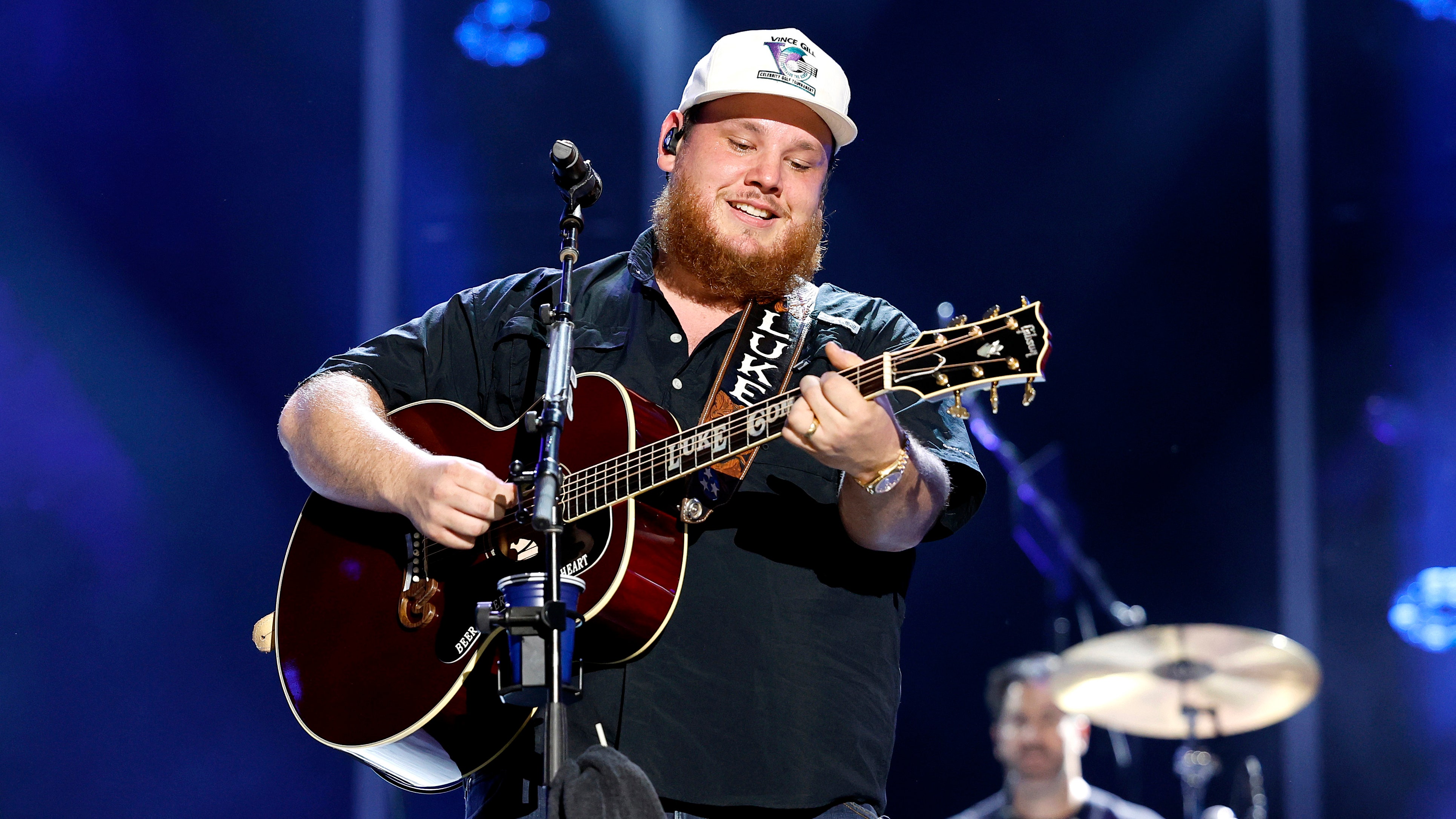 Luke Combs smiles as he looks down as his guitar while on stage