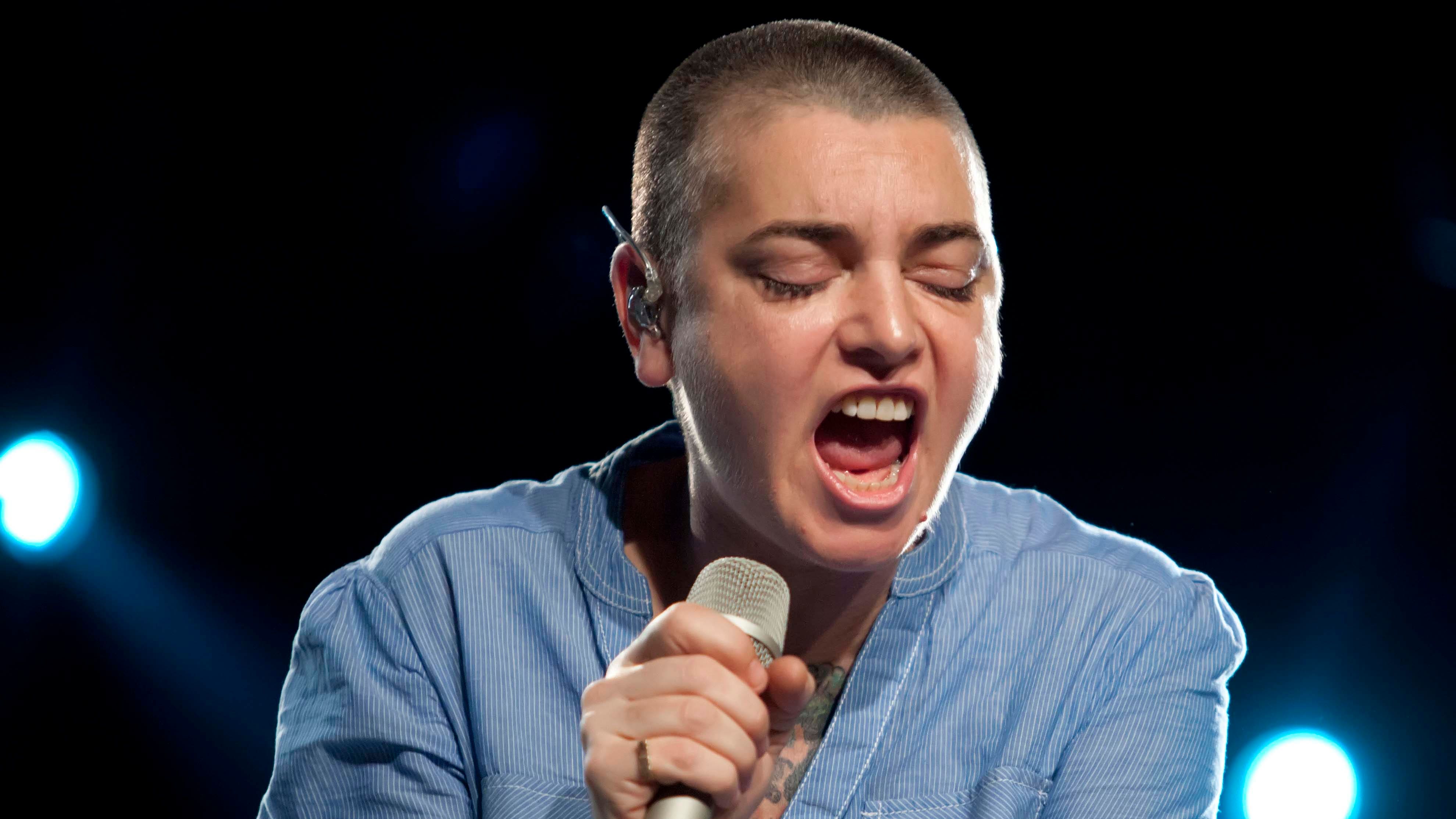 Sinéad OConnor wears a blue shirt and sings into the microphone in Berlin