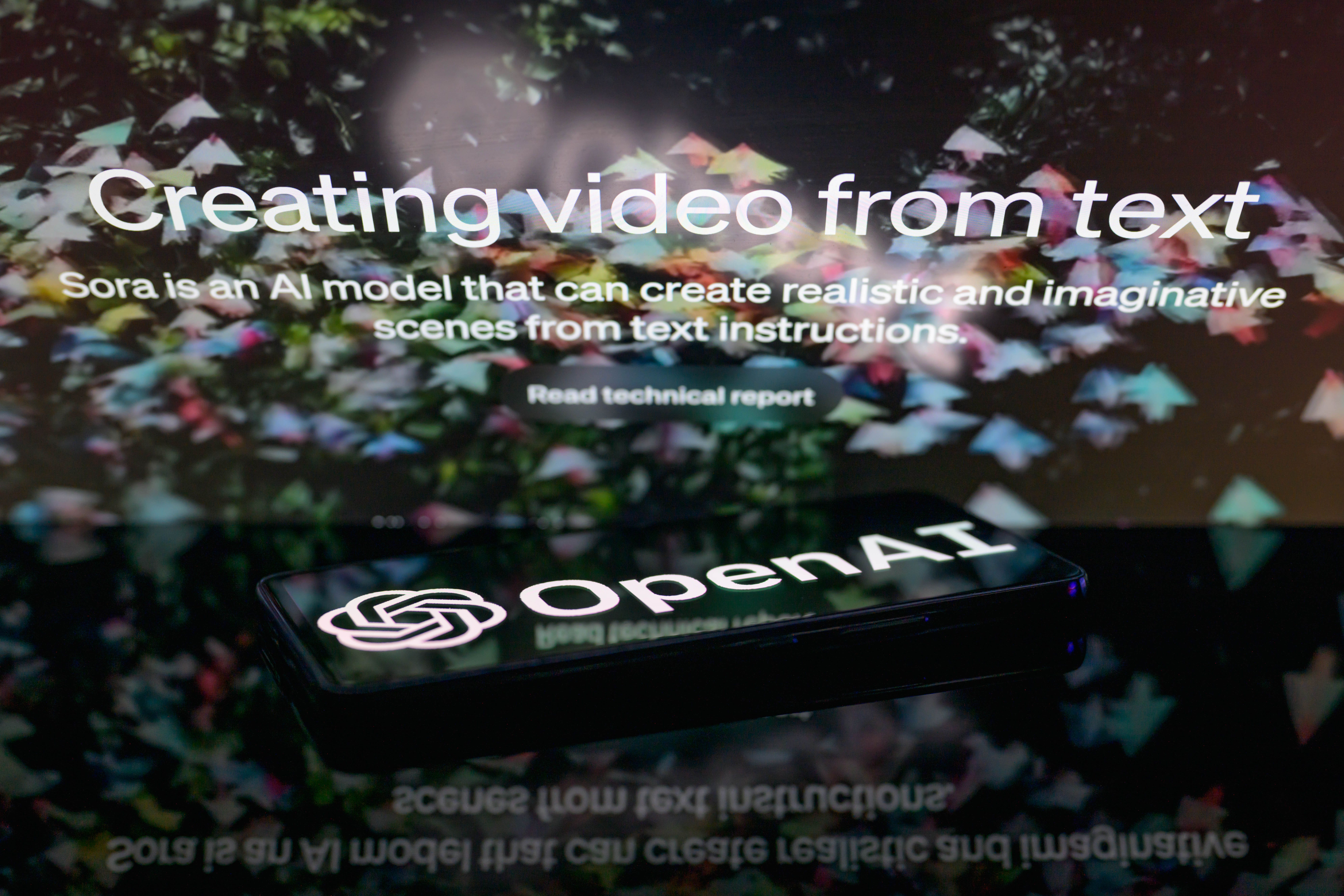 The OpenAI logo is being displayed on a smartphone with the Sora text-to-video generator visible in the background in this photo illustration, taken in Brussels, Belgium, on February 16, 2024. (Jonathan Raa/NurPhoto via Getty Images)