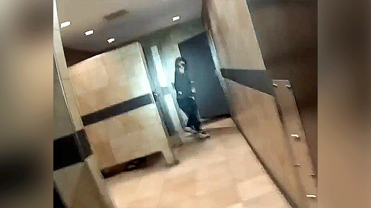 Suspect in black clothes and hoodie hold gun in restroom.